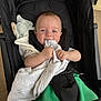 Leandros is registered to the contest to win money with this photo: baby, stroller, blanket, child, infant, smiling, clothing, green_pants, black_stroller, hands, face, blue_eyes, soft_toy, indoor, carpet, happy, cute, seated, comfort, portrait