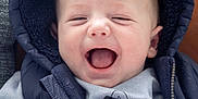 Leandros is registered to the contest to win money with this photo: baby, infant, smiling, laughing, hooded_vest, sweater, clothing, face, hand, mouth_open, happy, cute, child, portrait, indoor, cozy, warm, leather_background, person, casual