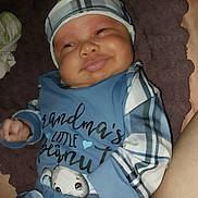 Niko is registered to the contest to win money with this photo: baby, infant, smile, plaid, hat, pajamas, cute, cozy, blanket, child, face, skin, hand, lying_down, happy, indoors, portrait, person, toddler, sleepwear