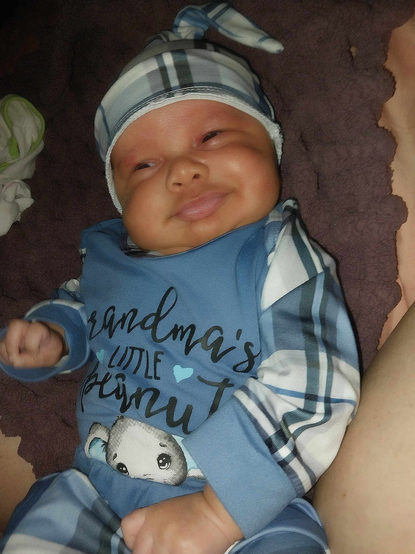 Niko is registered to the contest to win money with this photo: baby, infant, smile, plaid, hat, pajamas, cute, cozy, blanket, child, face, skin, hand, lying_down, happy, indoors, portrait, person, toddler, sleepwear