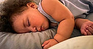 Oko is registered to the contest to win money with this photo: arm, baby, bed, blanket, child, clothing, cozy, curly_hair, face, indoors, infant, napping, peaceful, pillow, portrait, rest, skin, sleeping, soft_lighting, toddler