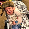 baby, child, smiling, stroller, blanket, fur_hat, indoor, toy_store, clothing, happy, portrait, infant, cute, warm, seated, colorful, accessory, fabric, comfort, playful