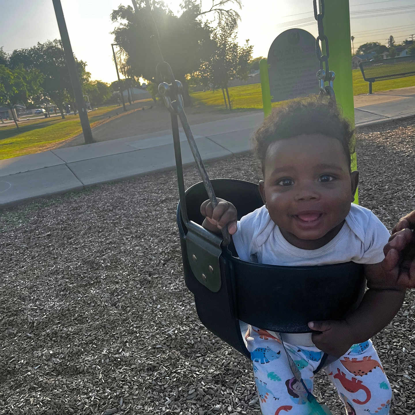 Rakai is registered to the contest to win money with this photo: baby, bench, child, clothing, daytime, dinosaur_pajamas, fun, grass, hand, happy, outside, park, person, play, playground, smiling, sunlight, swing, toddler, tree