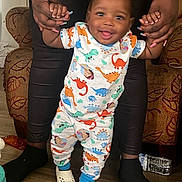 Rakai joined the competition — help win amazing prizes! baby, child, clothing, couch, dinosaur_pajamas, floor, footwear, furniture, hands, happy, home, indoor, nails, person, smile, support, toddler, walking, water_bottle, wooden_floor