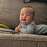 Zaire is registered to the contest to win money with this photo: baby, infant, child, smiling, sitting, couch, sofa, gray_clothing, sweater, blanket, pillow, phone, portrait, indoor, home, furniture, happy, face, baby_hands, close_up