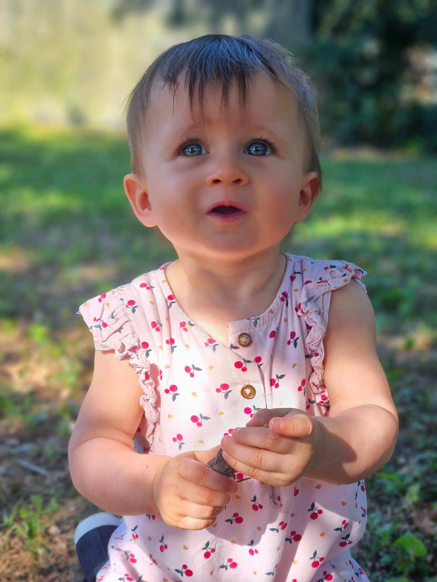 Albane a rejoint le concours — aidez-le/la à gagner de superbes lots ! toddler, child, outdoor, grass, dress, patterned_clothing, holding, stick, curious, blue_eyes, sunlight, nature, young_child, sitting, expression, portrait, summer, daylight, cute, innocence