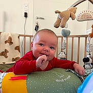 Lyam a rejoint le concours — aidez-le/la à gagner de superbes lots ! baby, blanket, child, cozy, crib, cushion, cute, face, hand, happy, indoor, infant, nursery, plush_toys, red_clothing, smiling, soft_toys, toddler, toy_mobile, wooden_crib