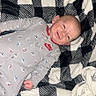 baby, infant, smiling, onesie, nike, blanket, checkered_pattern, gray_clothing, lying_down, cozy, indoors, cute, happy, child, young, person, soft_texture, fabric, casual, portrait