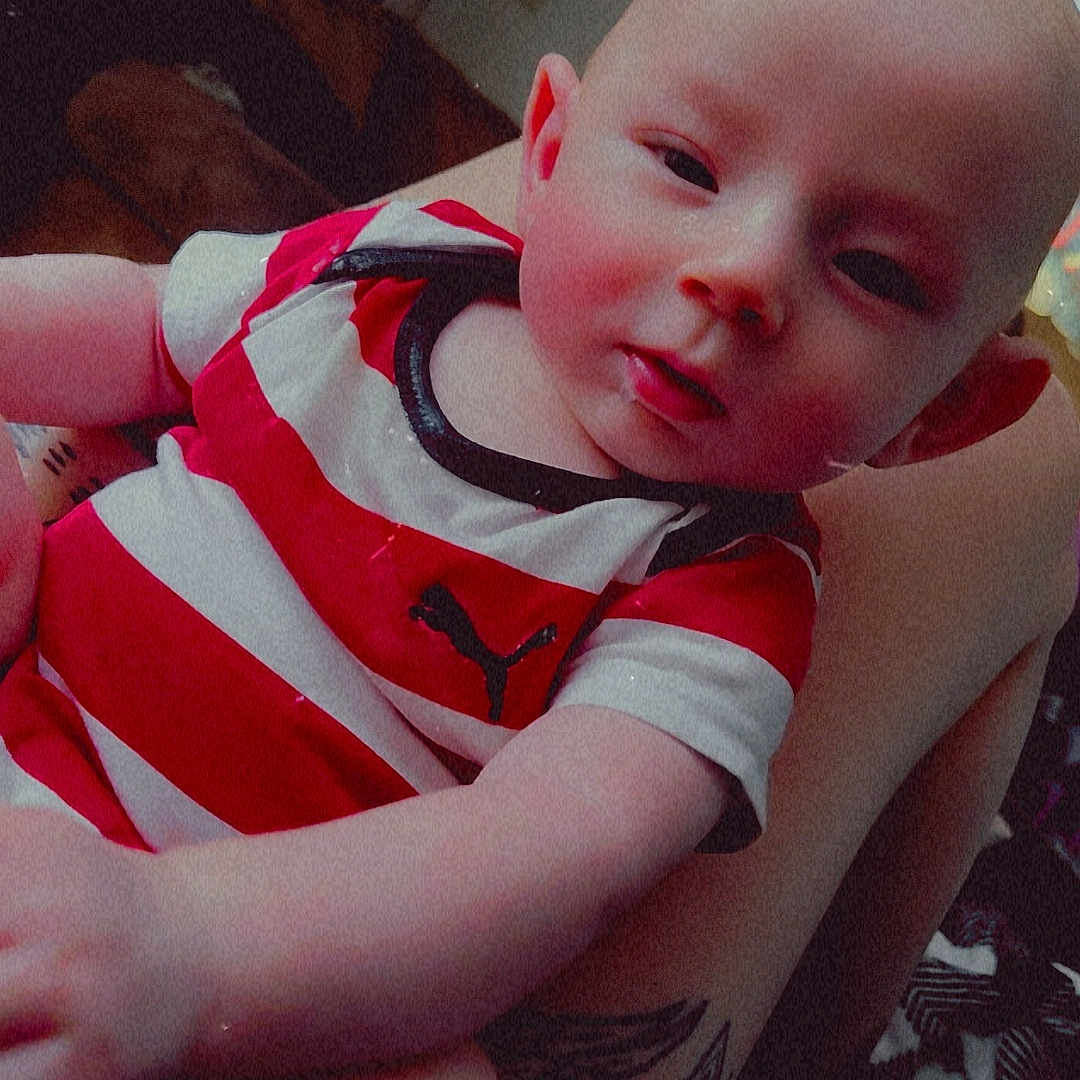 Achilles joined the competition — help win amazing prizes! baby, child, infant, striped_shirt, red, white, tattoo, arm, indoor, person, holding, face, skin, head, expression, clothing, baby_clothes, relaxed, sleepy, human
