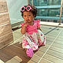 child, toddler, pink_sunglasses, curly_hair, floral_dress, pink_shoes, sunlight, shadow, tile_floor, outdoor, thinking, cute, sitting, baby, clothing, person, portrait, fashion, accessory, expression