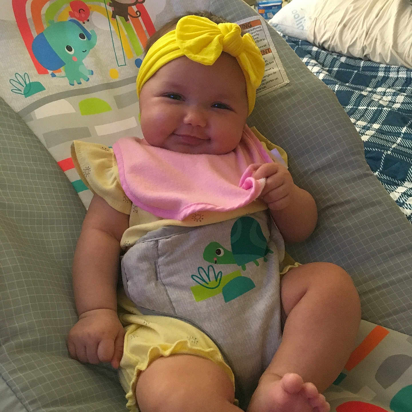 Ellieana is registered to the contest to win money with this photo: baby, infant, smile, yellow_headband, pink_bib, baby_seat, colorful, elephant, monkey, turtle, sun, indoor, cute, plush, child, clothing, happy, chubby_cheeks, person, portrait