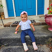 Nyree is registered to the contest to win money with this photo: toddler, child, smiling, portrait, outdoor, steps, blue_door, headband, toy, boots, concrete, plants, flower_pot, casual_clothing, happy, young_child, front_porch, candid, daylight, cute