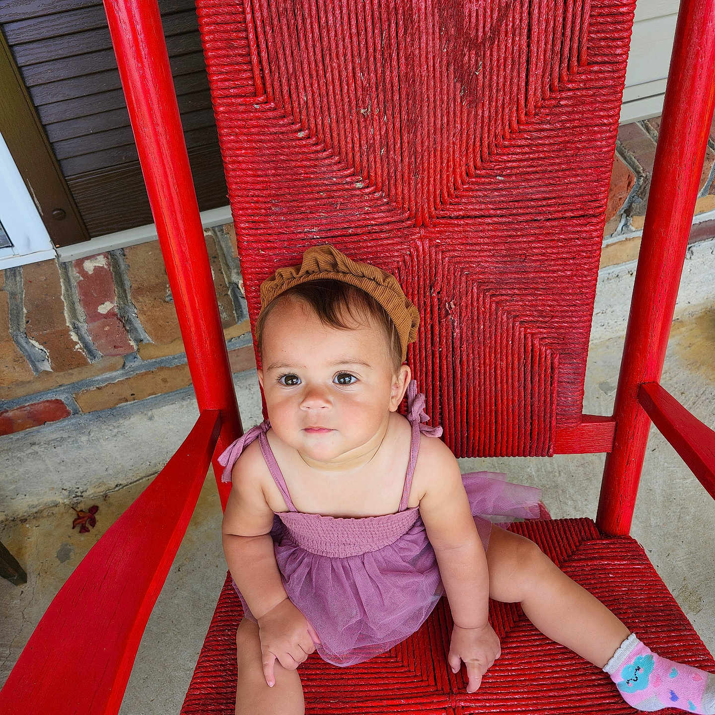Nyree joined the competition — help win amazing prizes! baby, brick_wall, casual, child, colorful, concrete_floor, cute, headband, outdoor, person, portrait, purple_dress, red_chair, relaxed, sitting, smile, socks, toddler, woven_chair, young_child