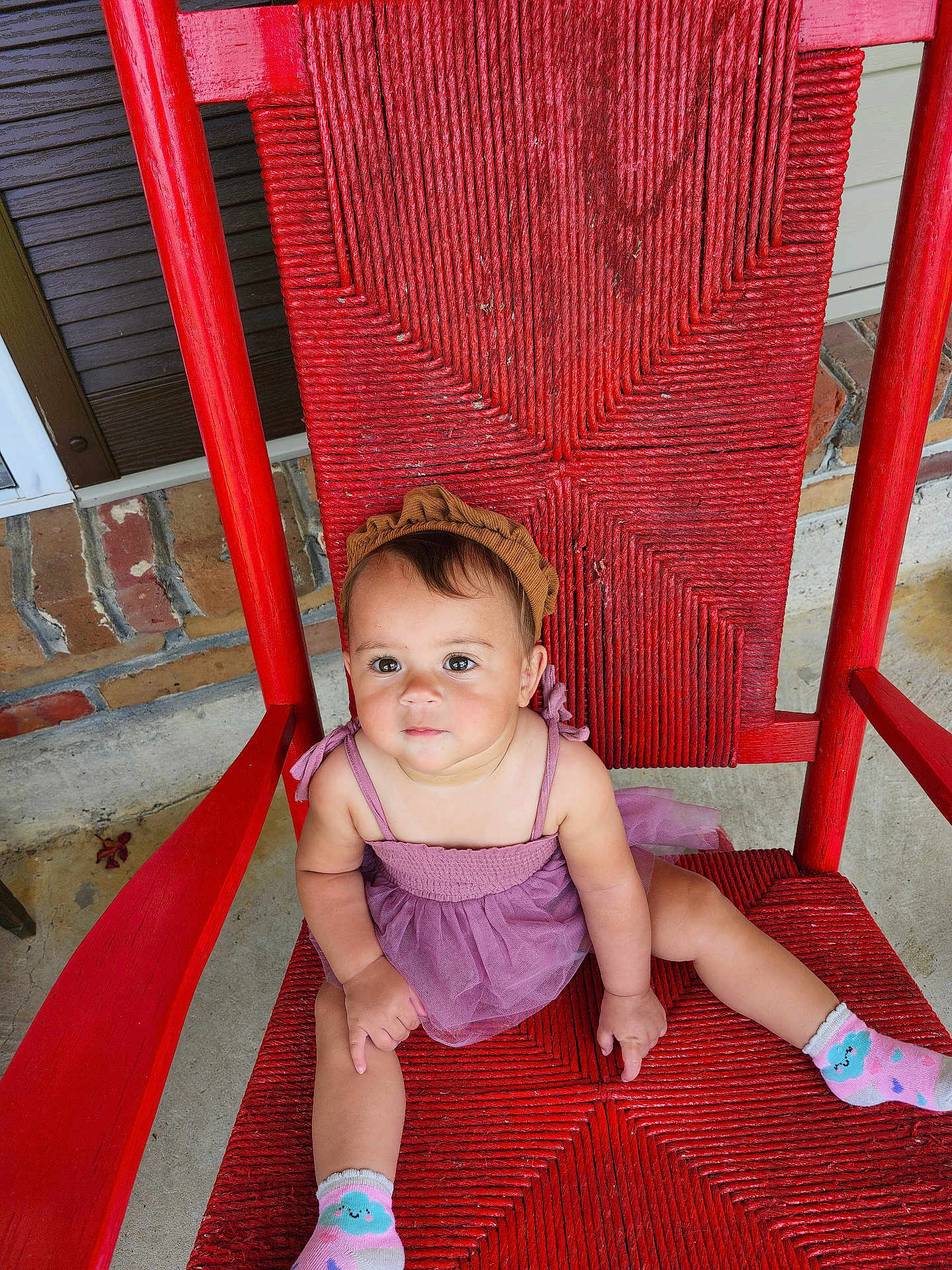 Nyree joined the competition — help win amazing prizes! toddler, child, red_chair, purple_dress, headband, socks, outdoor, brick_wall, concrete_floor, woven_chair, cute, sitting, portrait, baby, person, smile, relaxed, colorful, casual, young_child