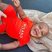 Kaizen joined the competition — help win amazing prizes! baby, smiling, red_onesie, blanket, happy, child, infant, face, skin, hand, foot, lying_down, soft_texture, clothing, cute, portrait, relaxed, indoors, baby_girl, baby_boy