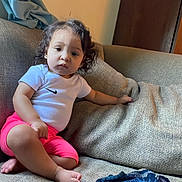 Juniper joined the competition — help win amazing prizes! toddler, child, curly_hair, white_tshirt, pink_shorts, sofa, couch, indoor, living_room, furniture, barefoot, person, young_child, casual_clothing, relaxed, seated, home, comfort, expression, portrait
