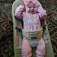 Kingston is registered to the contest to win money with this photo: baby, infant, pink_bow, pink_outfit, babybjorn, smiling, sneakers, carpet, indoor, child, cute, seated, headwear, footwear, person, happy, clothing, patterned_floor, baby_seat, portrait