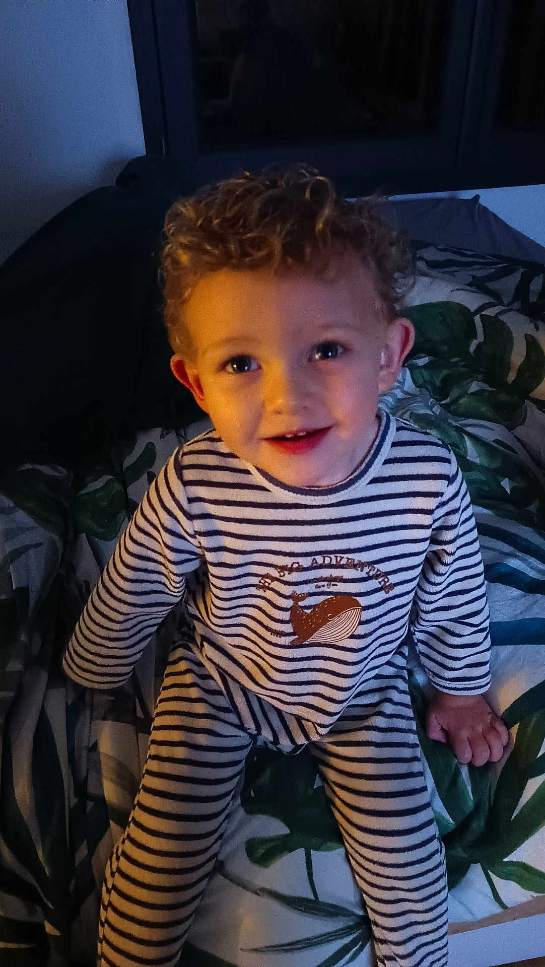Aryson participe au concours pour gagner de l'argent avec cette photo : child, toddler, curly_hair, striped_pajamas, whale_print, bed, bedspread, leaf_pattern, smiling, indoor, portrait, young_child, cute, happy, person, pajamas, cozy, home, evening_light, face