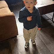 Aryson participe au concours pour gagner de l'argent avec cette photo : toddler, child, indoor, curly_hair, blue_eyes, hoodie, sweatpants, sneakers, curious, standing, brown_couch, wooden_table, papers, floor_tiles, lighting, backlight, person, clothing, young_child, casual_wear