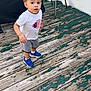 Ky Marshaun is registered to the contest to win money with this photo: toddler, child, curious, standing, outdoor, wooden_deck, peeling_paint, blue_sneakers, white_tshirt, gray_shorts, chair, covered_object, patriotic_emblem, casual, daylight, person, footwear, expression, young_child, background