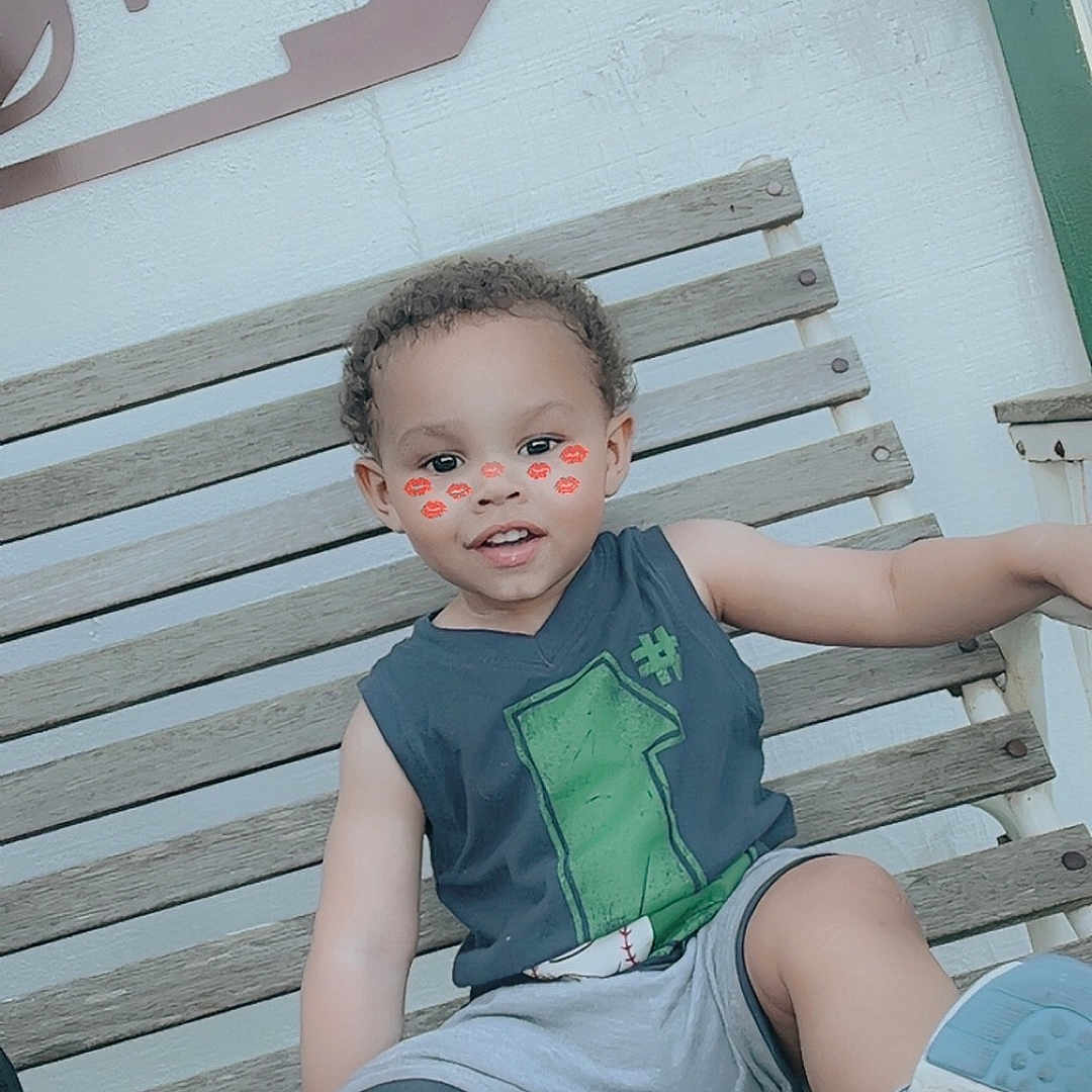 Ky Marshaun joined the competition — help win amazing prizes! bench, casual_clothing, child, curly_hair, cute, daytime, face_filter, happy, kiss_marks, outdoor, person, playful, relaxed, shorts, sitting, sleeveless_shirt, smiling, sneakers, toddler, wooden_bench