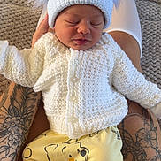 Arlo is registered to the contest to win money with this photo: baby, infant, hat, pom_poms, knitted_sweater, yellow_pants, bear_print, socks, tattoos, legs, sleeping, close_up, indoor, person, cute, cozy, resting, soft_texture, hand, warm_clothing