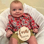 Kanon is registered to the contest to win money with this photo: baby, baby_photo, child, cute, face, four_months, happy, indoor, infant, khaki_shorts, person, plaid_shirt, portrait, red_clothing, sitting, smiling, soft_blanket, white_blanket, wooden_sign, young_child