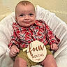 baby, baby_photo, child, cute, face, four_months, happy, indoor, infant, khaki_shorts, person, plaid_shirt, portrait, red_clothing, sitting, smiling, soft_blanket, white_blanket, wooden_sign, young_child