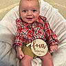 Kanon is registered to the contest to win money with this photo: baby, blanket, child, cozy, cute, face, four_months, hands, happy, indoors, infant, khaki_shorts, legs, plaid_shirt, portrait, sitting, smiling, white_blanket, wooden_sign, young_child