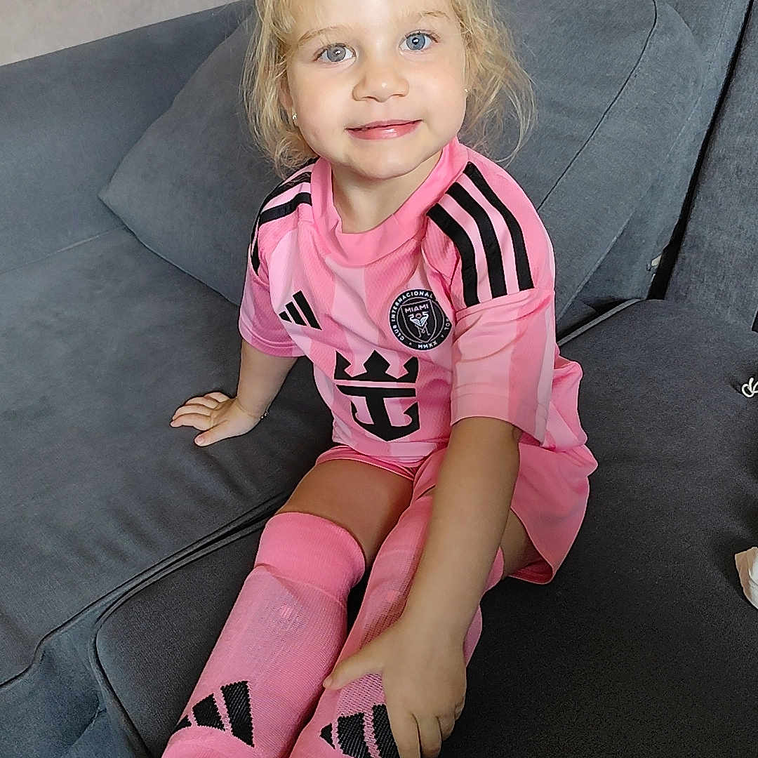 Théa participe au concours pour gagner de l'argent avec cette photo : blonde_hair, blue_eyes, casual, child, comfortable, couch, cushion, cute, girl, happy, home, indoor, person, pink_clothing, portrait, sitting, smiling, socks, sportswear, young