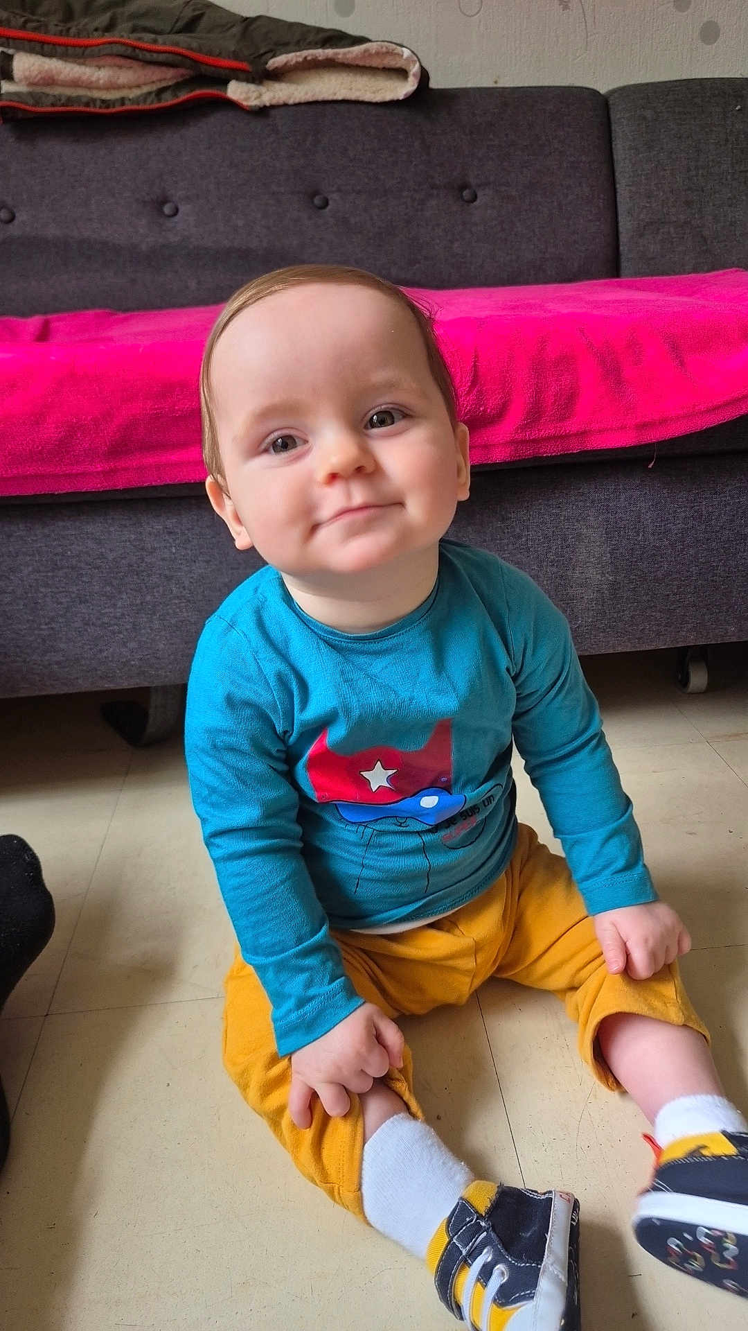 Kenzho participe au concours pour gagner de l'argent avec cette photo : toddler, child, smiling, sitting, floor, blue_shirt, yellow_pants, shoes, sock, face, indoor, couch, blanket, home, cute, happy, person, baby, casual, portrait
