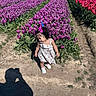 Kiki joined the competition — help win amazing prizes! toddler, child, flower_field, tulips, purple_flowers, red_flowers, sunlight, shadow, outdoor, nature, dress, hair_bows, plants, soil, pathway, daytime, person, greenery, scenic, summer