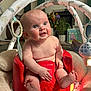 baby, infant, red_baby_seat, blue_eyes, baby_toys, indoor, plush_blanket, curious_expression, chubby_cheeks, soft_lighting, home_interior, plants, books, floor_play_area, child, cute, smiling, person, toy_hanger, cozy