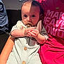 Brewer is registered to the contest to win money with this photo: baby, pacifier, infant, person, child, arm, clothing, shirt, text, red, green, buttons, face, hand, shadow, indoor, window, seated, closeup, holding