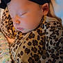 baby, sleeping, infant, headband, leopard_print, blanket, cozy, cute, child, soft, clothing, peaceful, face, portrait, indoors, newborn, rest, young_child, warm, snuggled