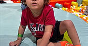 Stephen joined the competition — help win amazing prizes! child, toddler, curly_hair, red_shirt, jordan, orange_socks, ball_pit, play_area, indoor, padded_surface, colorful, casual_clothing, young_child, curious_expression, fun, kid, portrait, leisure, bright_colors, active