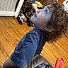child, curly_hair, blue_eyes, tshirt, gaming_controller, footwear, socks, red_sandal, wooden_floor, indoor, furniture, sneakers, toy, home, person, looking_up, side_profile, casual, room, living_space