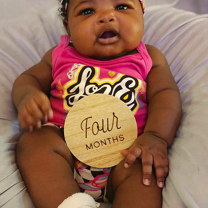 Miyonah joined the competition — help win amazing prizes! baby, child, closeup, colorful, curly_hair, cute, feet, four_months, hand, happy, headband, indoors, infant, legs, pink_clothing, portrait, smiling, socks, soft_surface, wooden_sign