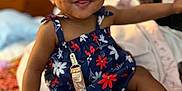 Talia is registered to the contest to win money with this photo: baby, child, smiling, happy, sitting, bed, blanket, clothing, footwear, red_socks, white_shoes, hair_buns, dimples, face, indoor, pacifier, colorful, patterned, cute, person