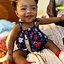 baby, child, smiling, happy, sitting, bed, blanket, clothing, footwear, red_socks, white_shoes, hair_buns, dimples, face, indoor, pacifier, colorful, patterned, cute, person