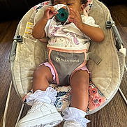 Talia joined the competition — help win amazing prizes! baby, child, infant, rocker, baby_gear, white_shoes, socks, bow, hair_accessory, unicorn_shirt, pink_shorts, indoor, wooden_floor, couch, polka_dot, playing, smiling, person, seat, comfortable