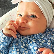 Camille a rejoint le concours — aidez-le/la à gagner de superbes lots ! baby, baby_girl, blue_eyes, bow, child, close_up, clothing, cute, floral_pattern, hand, happy, headband, indoors, infant, lying_down, person, portrait, skin, smile, soft_surface