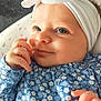 baby, baby_girl, blue_eyes, bow, child, close_up, clothing, cute, floral_pattern, hand, happy, headband, indoors, infant, lying_down, person, portrait, skin, smile, soft_surface