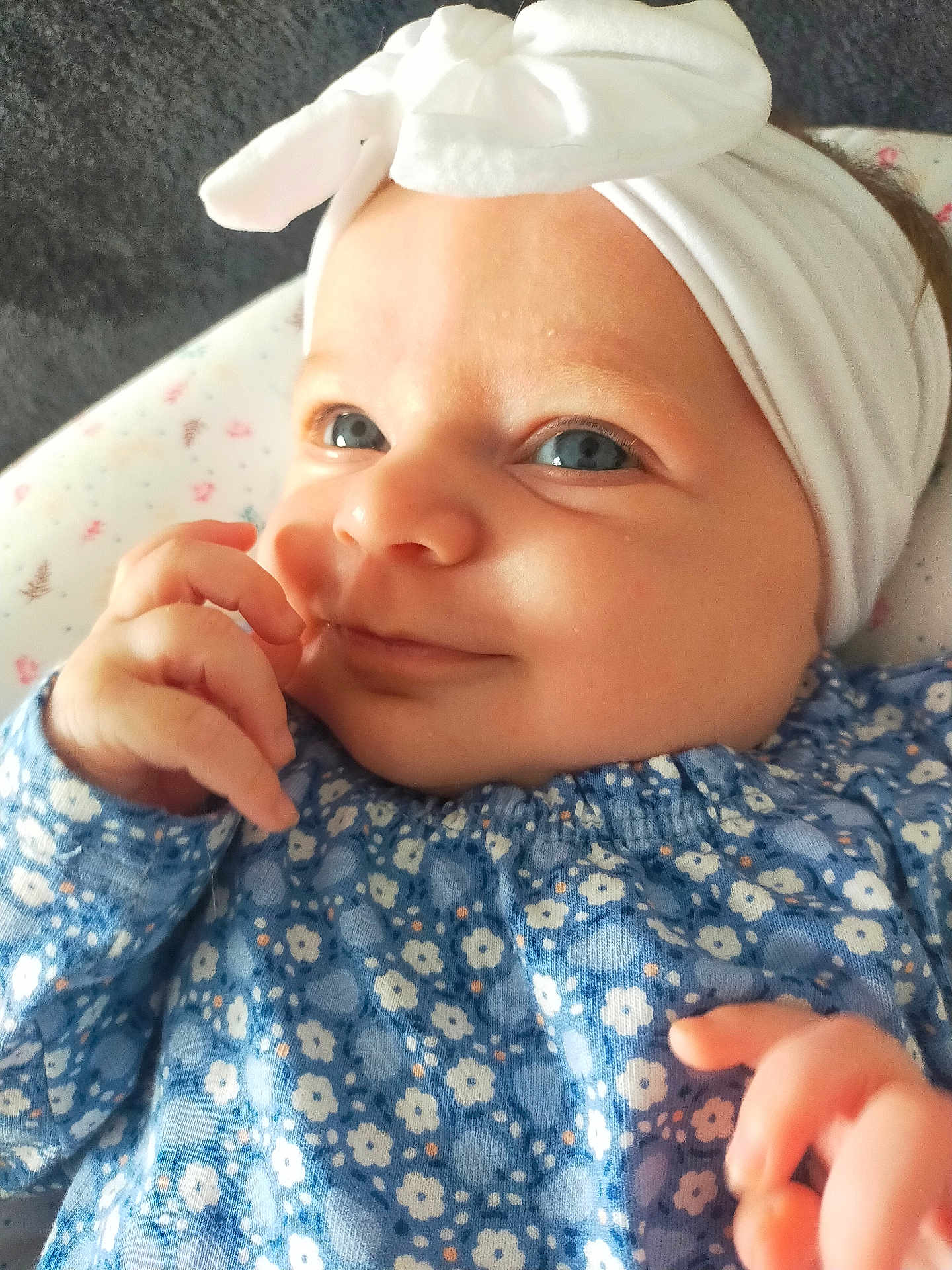 Camille a rejoint le concours — aidez-le/la à gagner de superbes lots ! baby, baby_girl, blue_eyes, bow, child, close_up, clothing, cute, floral_pattern, hand, happy, headband, indoors, infant, lying_down, person, portrait, skin, smile, soft_surface