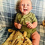 Waylon joined the competition — help win amazing prizes! baby, smiling, plaid_blanket, green_clothing, teddy_bear, stuffed_animal, chubby_cheeks, happy, infant, sitting, cozy, soft_toy, cute, portrait, child, indoors, blanket, hand, face, light