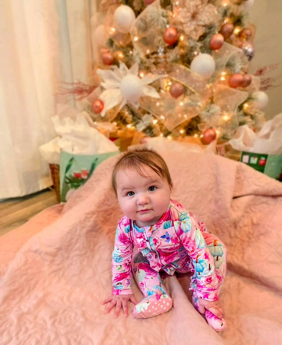 Sasha joined the competition — help win amazing prizes! baby, child, infant, pajamas, pink_blanket, christmas_tree, ornaments, lights, holiday, indoor, curious, sitting, decorations, floor, present, gift_bags, festive, cute, face, person