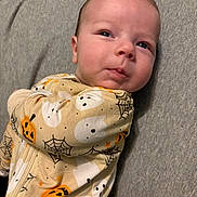 Asher is registered to the contest to win money with this photo: baby, infant, onesie, halloween, pumpkin, ghost, spiderweb, clothing, face, expression, lying_down, soft_surface, cute, child, portrait, indoors, sleepwear, newborn, person, head