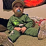 toddler, child, pacifier, cap, green_clothing, dinosaur_print, indoor, carpet, blanket, tapestry, shoe, sitting, cute, face, person, footwear, casual, young_child, home, relaxed
