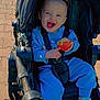 Oceanna joined the competition — help win amazing prizes! toddler, child, stroller, blue_clothing, apple, smiling, happy, outdoor, sunlight, pavement, shoes, seatbelt, baby, cute, person, playful, daytime, casual, young_child, sitting