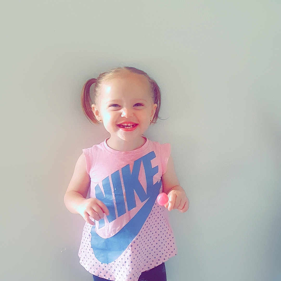 Oceanna is registered to the contest to win money with this photo: casual_clothing, child, cute, floor, girl, happy, heart_pattern, indoor, lollipop, nike, person, pigtails, pink, shorts, smiling, standing, toddler, tshirt, wall, white_sneakers